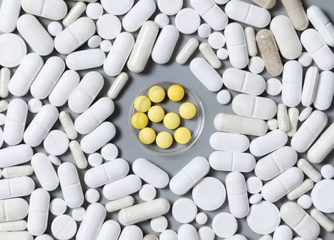 Mix of white medical capsules and pills with yellow pills in the middle on grey top view. Medicinal treatment. Taking dietary supplements. Assorted pharmaceutical products