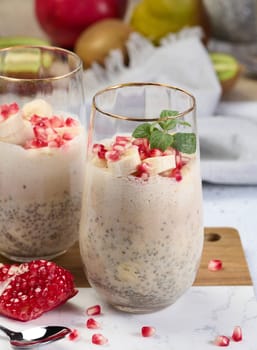 A glass of chia seeds and yogurt, with banana pieces and pomegranate seeds added to the dessert
