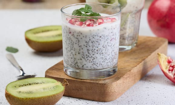 Two glasses of chia yogurt dessert garnished with fresh fruit, pomegranate seeds and kiwi slices