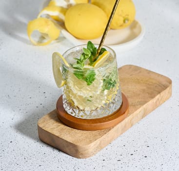 Transparent glass with lemon slices, mint leaves and ice cubes on white table