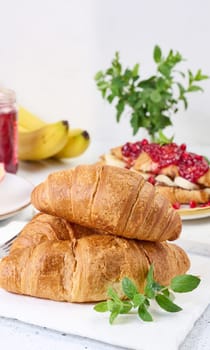 Baked croissants, jam and pomegranate on white table, breakfast