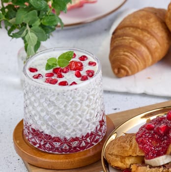 Glass of yogurt with chia seeds, pomegranate seeds and baked croissants on table