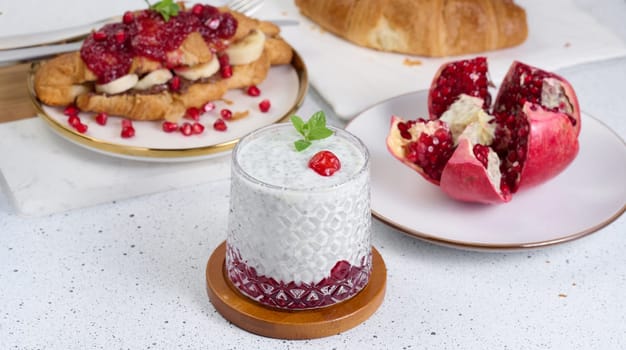 Glass with chia and yogurt dessert decorated with green mint leaf on white table