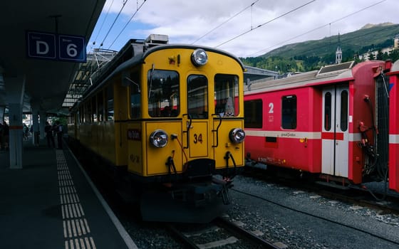 St. Moritz, Switzerland August 11 2021: A vibrant summer scene at St. Moritz station with vintage yellow and red trains set against the picturesque Swiss Alps in Graubunden, Switzerland