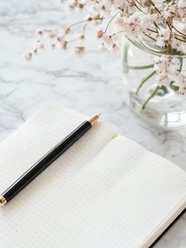 Elegant minimalist desk setup with an open notebook and delicate flowers on a marble surface, ideal for writing.