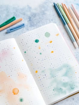 Open notebook with watercolor splashes and colorful pens, perfect for artistic expression and creativity.