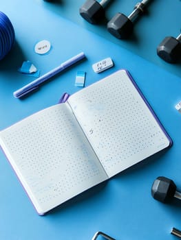 A fitness journal surrounded by exercise equipment on a blue background, ideal for workout planning.