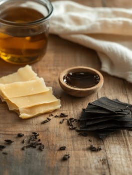 Arrangement of honey, wax, and dark leaves on a wooden table, showcasing natural materials.