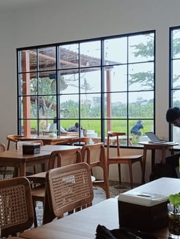 A cozy cafe interior featuring wooden furniture with a large window overlooking a serene garden. The peaceful atmosphere is ideal for relaxation and work.