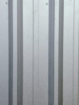 A close-up view of a corrugated metal wall featuring red trim, highlighting industrial design and texture. The metallic sheen contrasts with the reddish hue, offering a modern yet rustic feel.