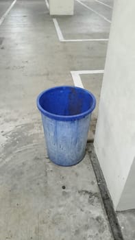 A lone blue plastic trash bin stands in an empty parking garage. The concrete surroundings create a stark, urban atmosphere. Ideal for themes of waste management and urban living.
