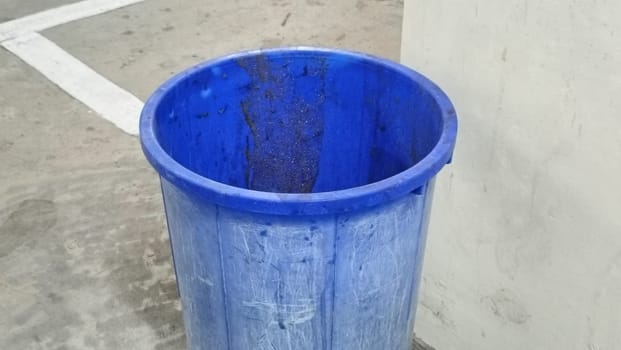 A lone blue plastic trash bin stands in an empty parking garage. The concrete surroundings create a stark, urban atmosphere. Ideal for themes of waste management and urban living.
