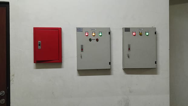 Image of a red fire safety box and two electrical control panels mounted on a plain white wall. Highlights industrial and safety equipment in a controlled environment.