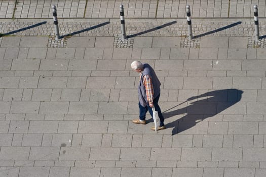 old pensioner on a footpath in a pedestrian zone with text space on the left side