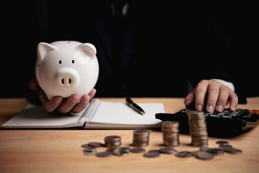 Hand holding a piggy bank with coins and calculator on the desk. Suitable for savings, financial planning, and investment topics.