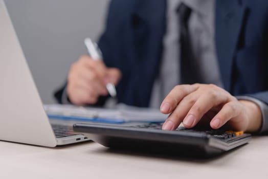 Businessman using calculator with documents and laptop on desk. Represents financial management, budgeting, accounting, and economic planning.