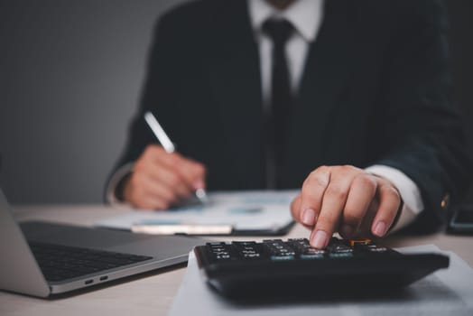 Close-up of a businessman in a suit working at a desk. Hand pressing calculator, analyzing documents. Professional, focused on financial calculations. Suitable for business, finance