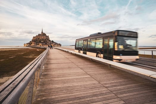 Mont Saint-Michel, France - February 25, 2024: Mont Saint-Michel and shuttle bus with tourists photographed in winter from the long bridge in Normandy, France