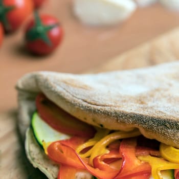 Closed calzone pizza on rustic wooden background. On background small red tomatoes, mozzarella and basil. Italian food. Selective focus.