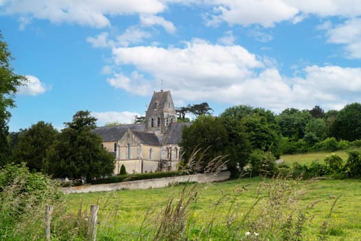 A church with a steeple sits in a grassy field. The sky is clear and blue, and the sun is shining brightly. Normandy, France