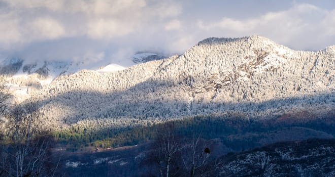 A mountain range covered in snow with a bright sun shining on it. The sun casts a shadow on the snow, creating a beautiful and serene scene