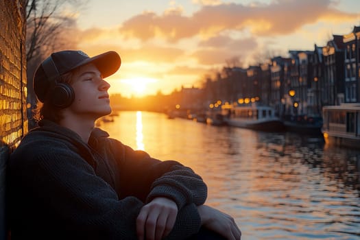A young man leaning against a wall near the canals, wearing an oversized sweater and a baseball cap, listening to music through his vintage headphones. AI generative.