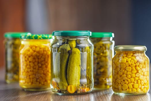 Canned vegetable. Pickled corn, cucumbers and jalapeno peppers on a wooden table.