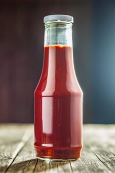 Glass bottle of ketchup on a wooden table.