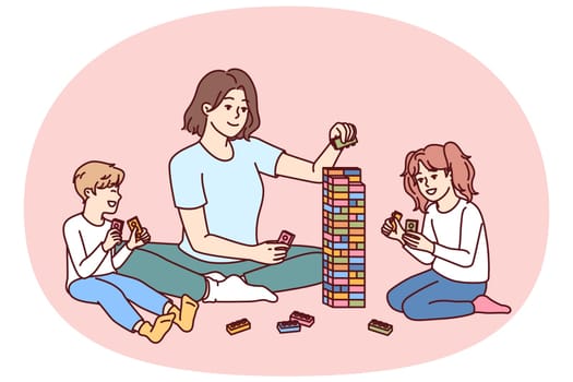 Woman babysitter together with kids plays constructor building tower of children blocks in kindergarten. Little boy and girl have good time and play educational games under supervision of babysitter