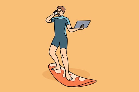 Business man works standing on surfboard, with laptop and mobile phone in hands. Happy guy in diving suit uses surfboard and freelancing gadgets at same time, working while on vacation.