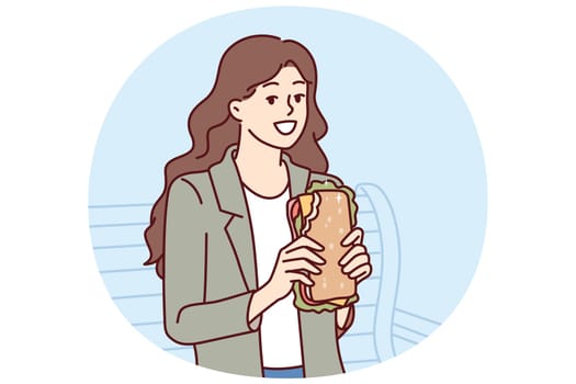 Woman eats sandwich while sitting on bench in park and enjoying street food and good weather. Young smiling city girl with cheese sandwich takes break from walking to eat and gain strength