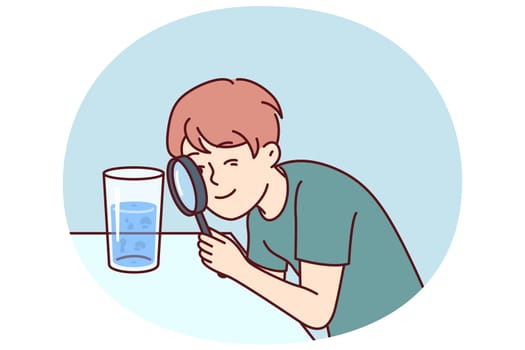 Small boy examines water in glass through magnifying glass, studying chemical composition liquid or looking for microbes. Teenage child curiously studies water, wanting to work in chemical laboratory