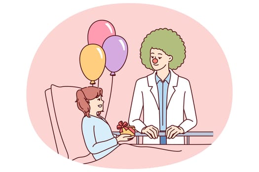 Clown doctor gives gift to child who is in hospital and needs support and positive emotions. Caring doctor pediatrician stands near bed with little girl undergoing rehabilitation in children hospital