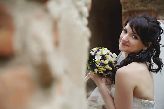 Stunning bride elegantly poses with her bouquet in the ruins of an old fortress outdoors