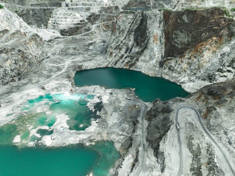 Large limestone quarry operation. Industrial trucks working at open pit mining site with striking turquoise water. Resource extraction process. Mining operation in limestone quarry. Industrial scale.
