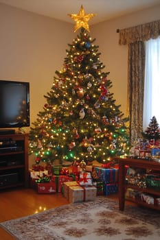 A beautifully decorated Christmas tree stands brightly lit, surrounded by numerous presents in a cozy living room setting.