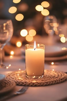 A beautifully arranged table features a lit candle, creating a warm and inviting atmosphere with soft glowing lights in the background.