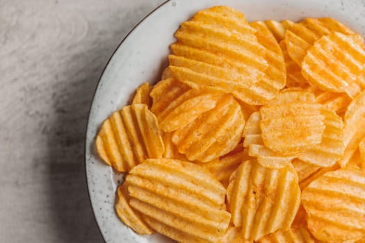 Crispy potato chips on plate on a kitchen table. Top view.