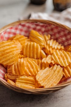 Crispy potato chips in basket on a kitchen table.