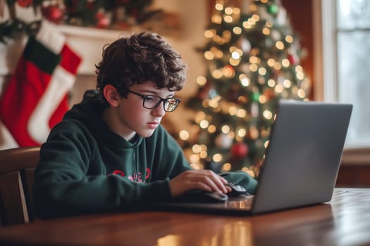 A young boy sits at a wooden table using a laptop, immersed in work, with a decorated Christmas tree in the background.