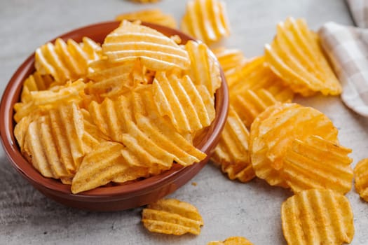 Crispy potato chips in bowl on a kitchen table.