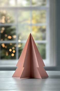 A handcrafted paper tree stands on a table, illuminated by soft natural light and festive decor visible outside the window.