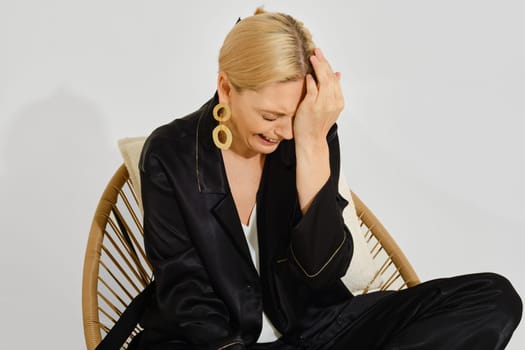 A woman enjoys a lighthearted moment while seated in a stylish chair, laughing with her hand on her forehead. The soft natural light enhances her joyful expression and relaxed atmosphere.