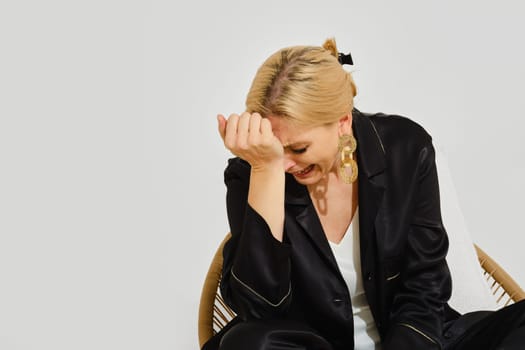 A woman is crying while sitting dramatically in a chair, her vibrant expression reflecting sadness in a well-lit indoor environment