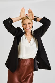 A woman expresses her playful side by making cheerful gestures with her hands, wearing an elegant outfit.