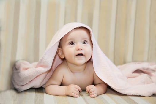 An adorable baby is looking up with wonder while being covered snugly by a soft pink blanket thats cozy