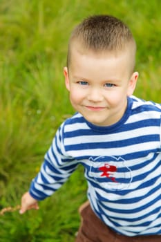 A joyful little boy with a big smile and a striped T-shirt is playing outside