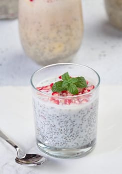 Glass with chia and yogurt dessert decorated with fresh fruits and pomegranate seeds on white table