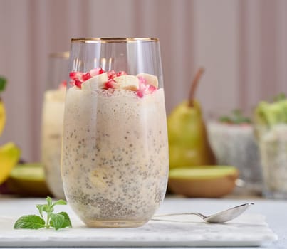 A glass of chia seeds and yogurt, with banana pieces and pomegranate seeds added to the dessert
