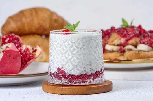 Glass with chia and yogurt dessert decorated with green mint leaf on white table